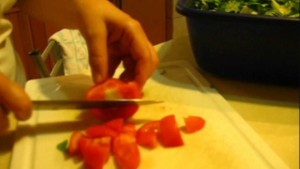 A close-up picture of a hand and knife cutting up a tomato.